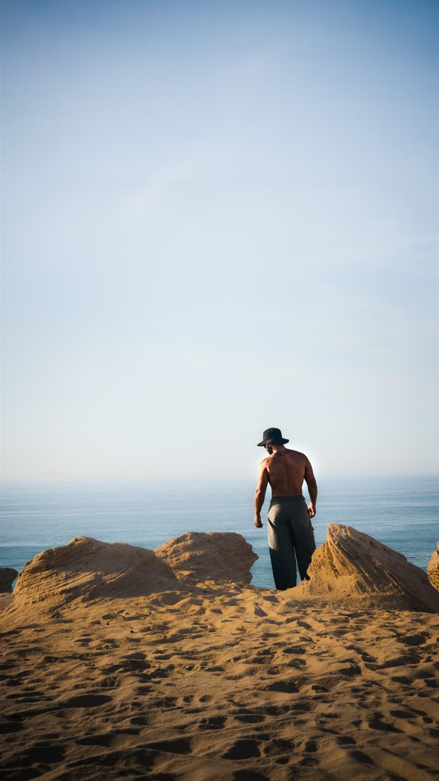 Adam on a sand cliff facing the ocean